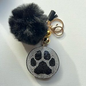 Llavero (Keychain) con pompón y huella de mascota en color negro.